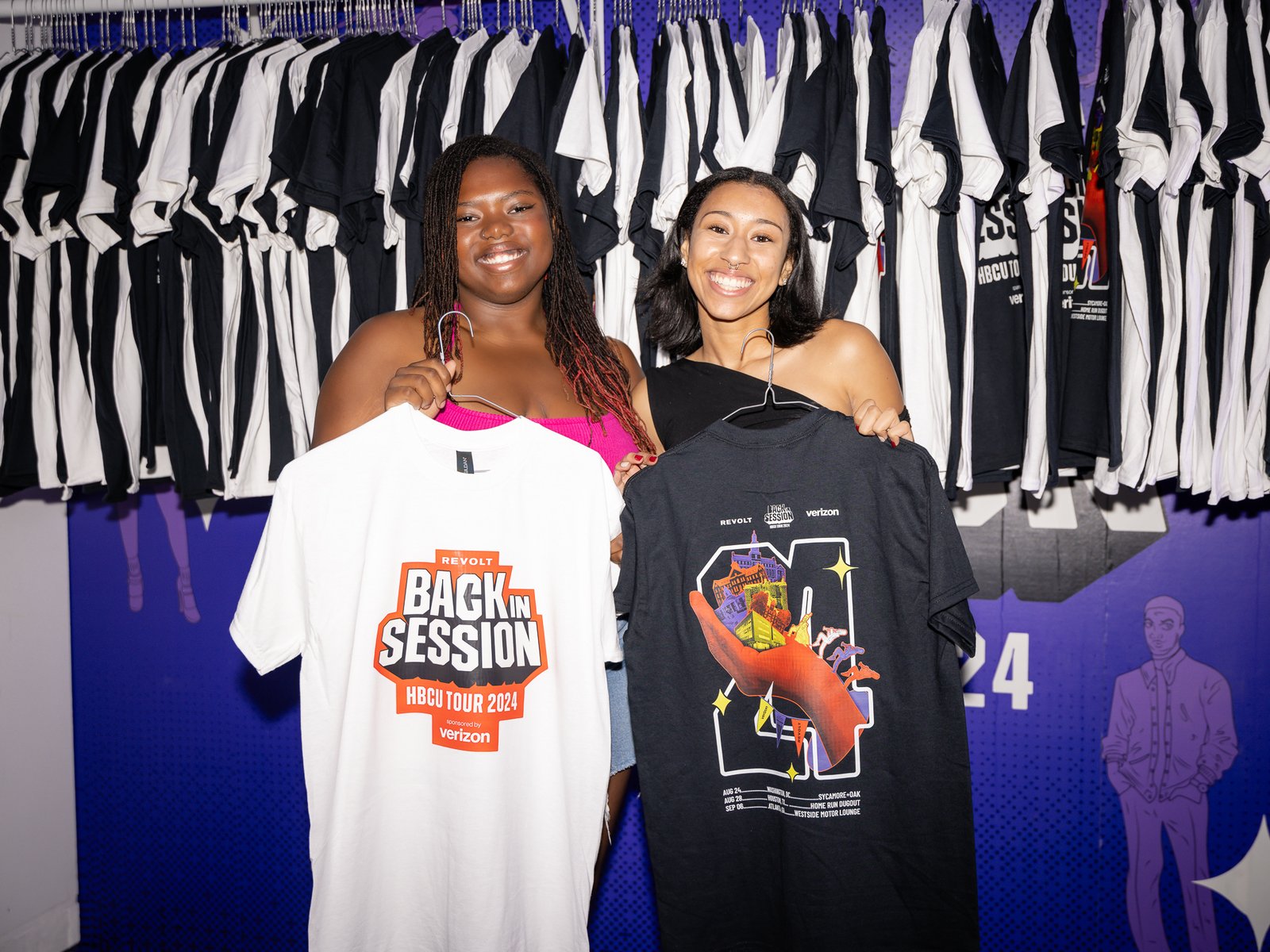 Two students holding Back In Session HBCU Tour 2024 shirts in front of the merch wall