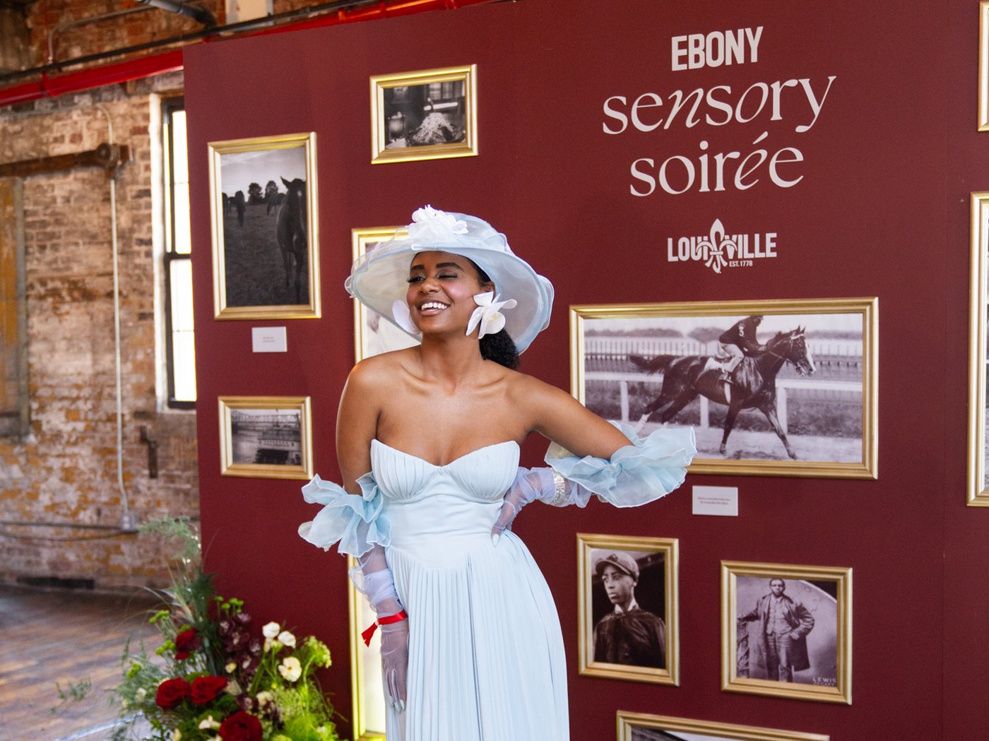 Guest in Derby attire in front of the EBONY Sensory Soirée wall with framed horse racing history photos